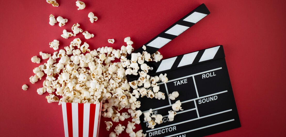 Popcorn und eine Filmklappe vor rotem Hintergrund