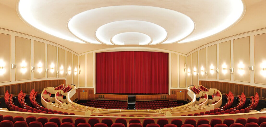 Großer Kinosaal mit Bühne und roten Stühlen