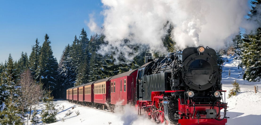 Historischer Dampfzug fährt durch eine verschneite Landschaft