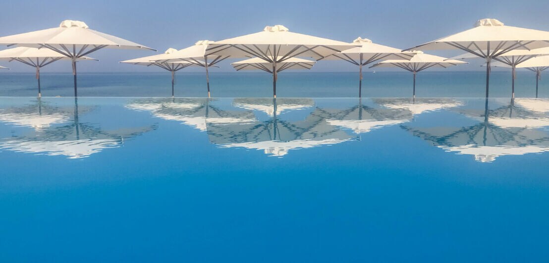 Sonnenschirme spiegeln sich in einem Infinity-Pool
