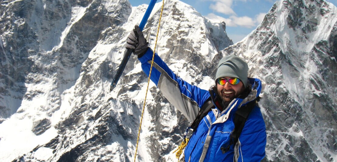 Ein Bergsteiger mit Ausrüstung vor einem schneebedeckten Berg