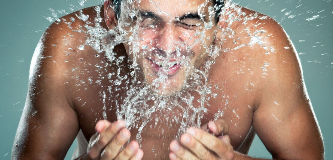 Ein Mann kühlt sein Gesicht mit kaltem Wasser.