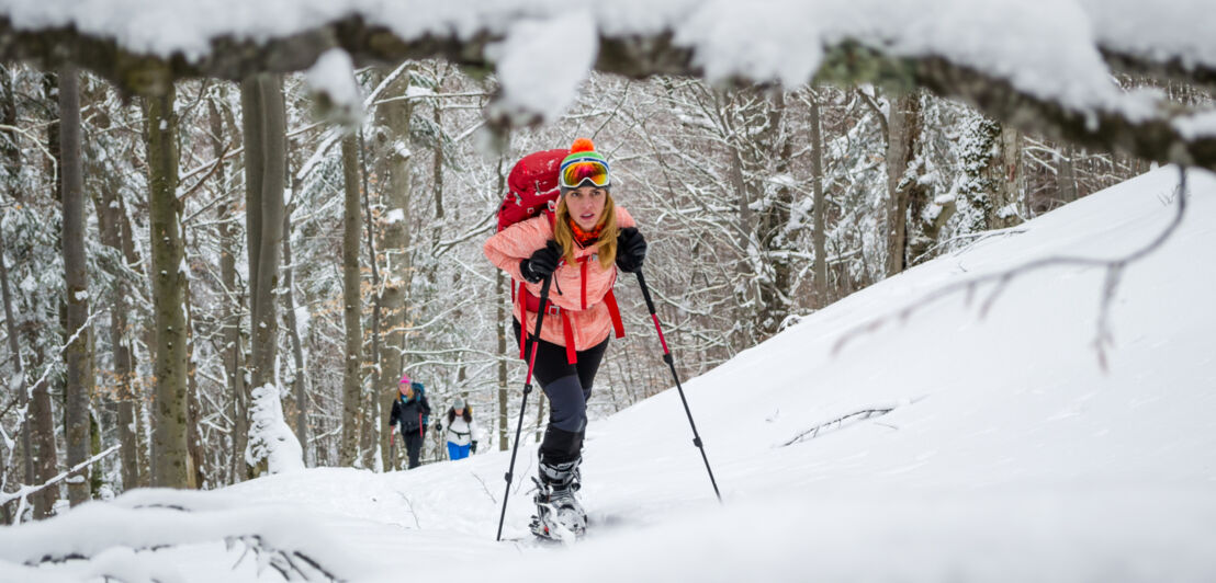 Eine Frau in Skibekleidung geht einen schneebedeckten Berg hinauf