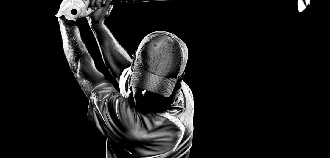 Schwarz-Weiß-Aufnahme eines Golfspielers beim Abschlag vor schwarzem Hintergrund