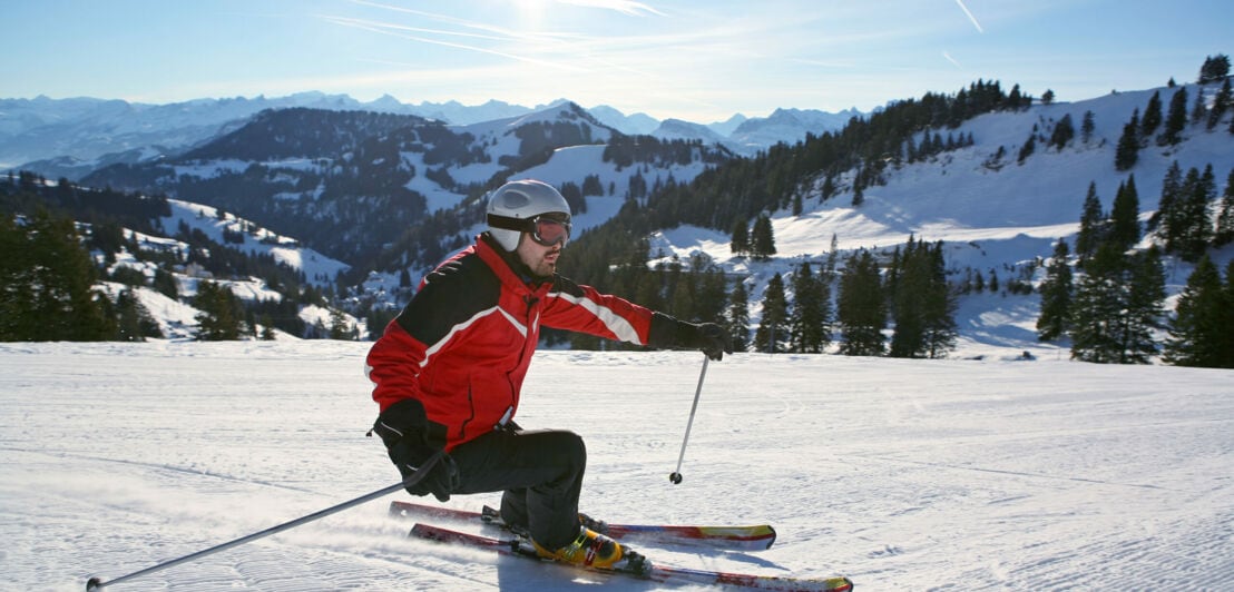 Ein Mann auf Skiern fährt einen verschneiten Berg hinunter.