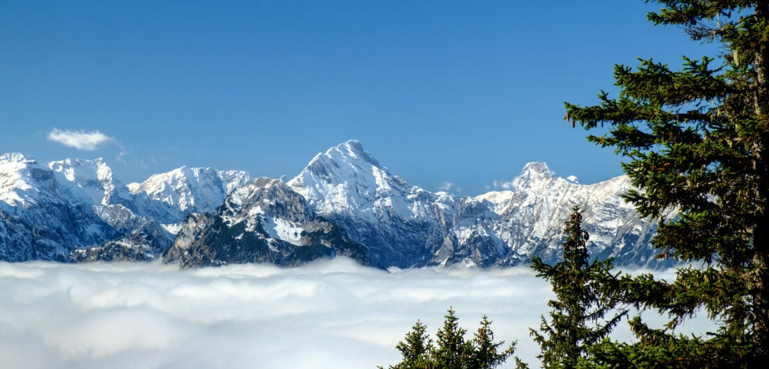 Panoramaansicht auf das Karwendelgebirge mit verschneiten Gipfeln vor strahlend blauem Himmel und dichter Wolkendecke zum Tal hin