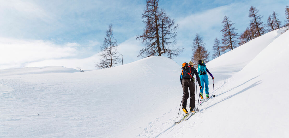 Zwei Menschen mit Skiausrüstung wandern auf Ski einen Schneeberg hoch