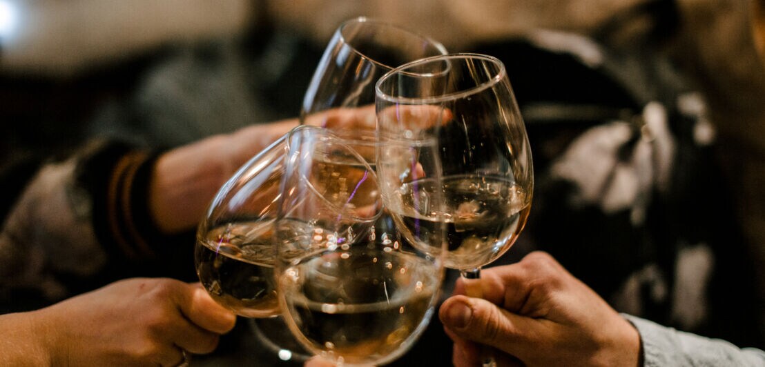 Vier Menschen toasten sich mit Weingläsern in der Hand zu.