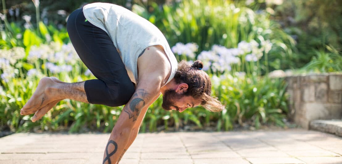 Ein sportlicher Mann macht eine Yogaübung im Grünen