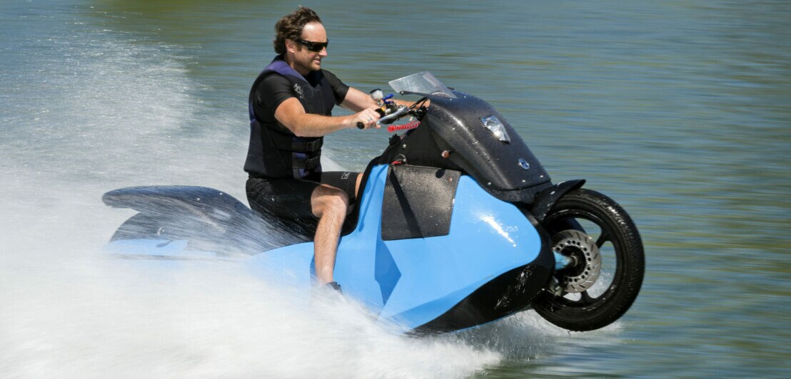 Ein Mann fährt mit einem Amphibienfahrzeug (halb Motorrad, halb Jetski) auf dem Wasser