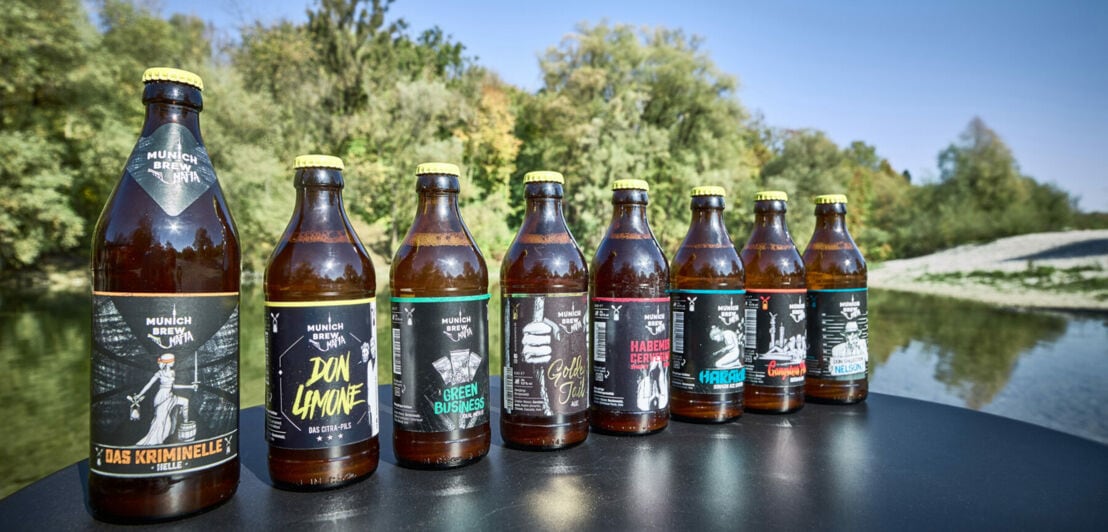 Eine Reihe Bierflaschen mit modern designten Labels auf einem Tisch an einem See