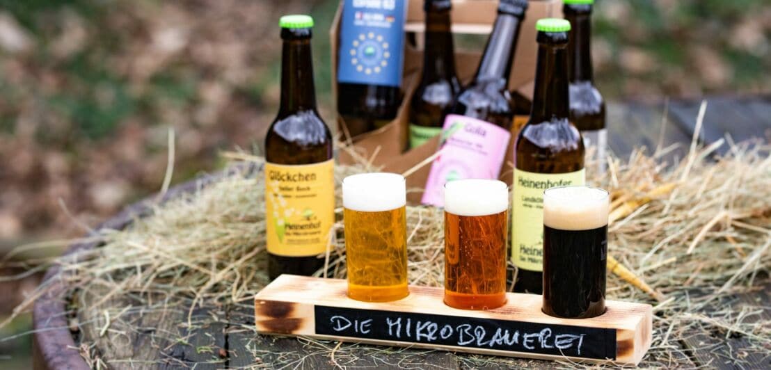 Bierflaschen und drei Sorten Bier sind auf einem Holzfass arrangiert