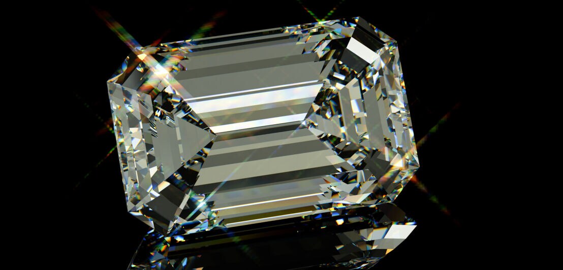 Ein Diamant mit Smaragdschliff vor schwarzem Hochglanz-Hintergrund.