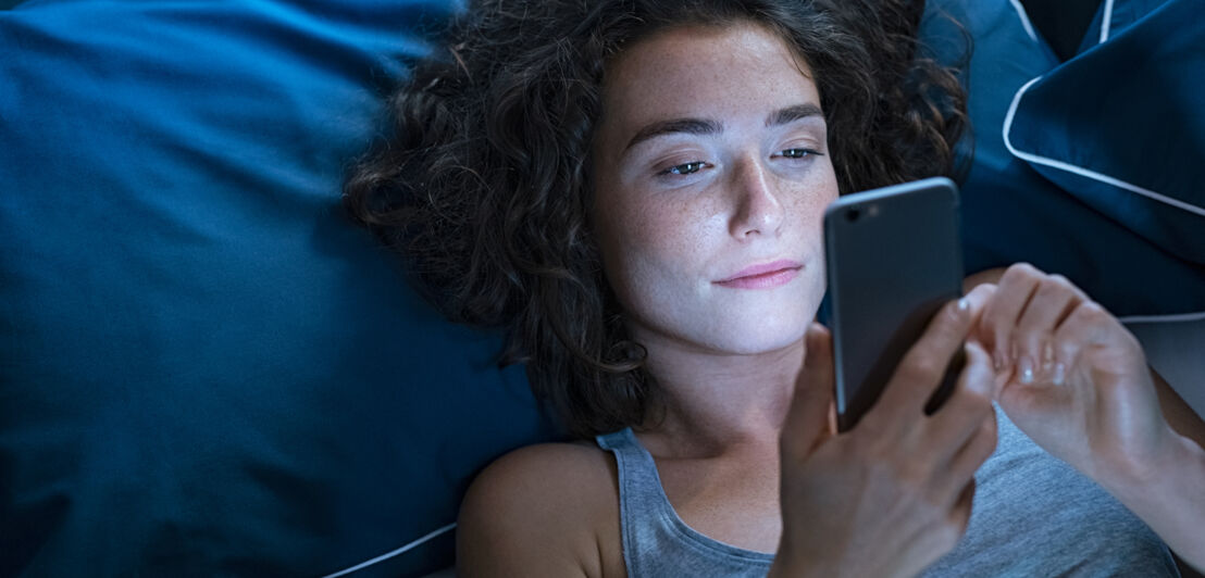 Eine Frau liegt im Bett und schaut auf ihr Smartphone