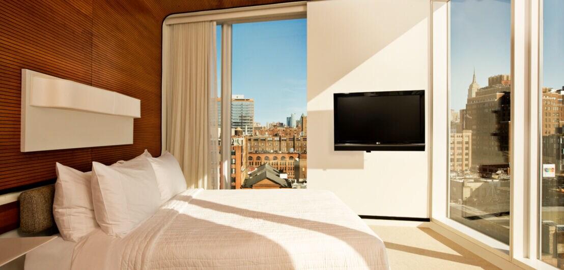 Ein Hotelzimmer mit großen Fenstern, durch die Hochhäuser zu sehen sind