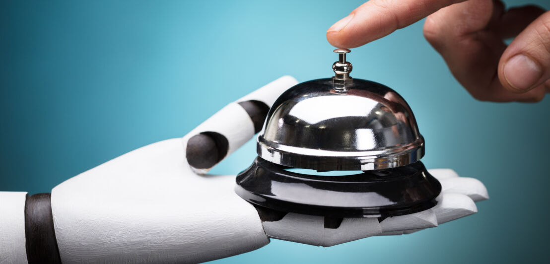 Eine Hand drückt eine Tischklingel, die eine Roboterhand hält