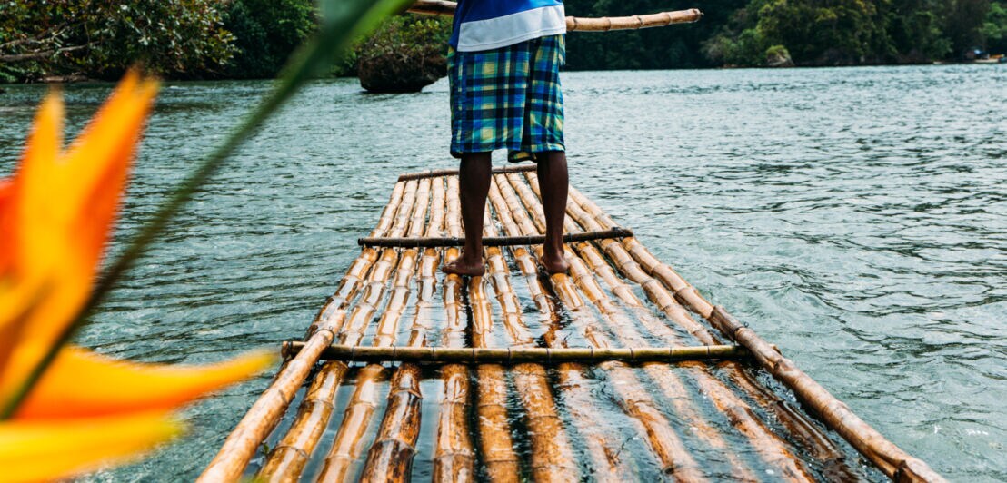 Ein Mann steuert auf einem Bambusfloß über einen Fluss