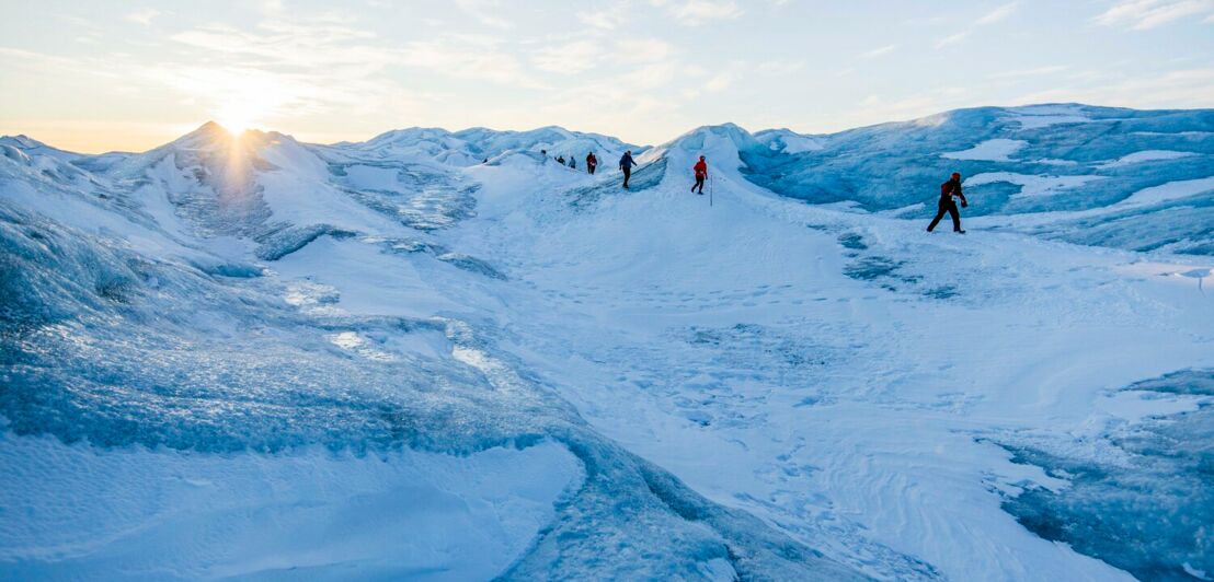 Menschen laufen über eine vereiste hügelige Landschaft in Grönland.
