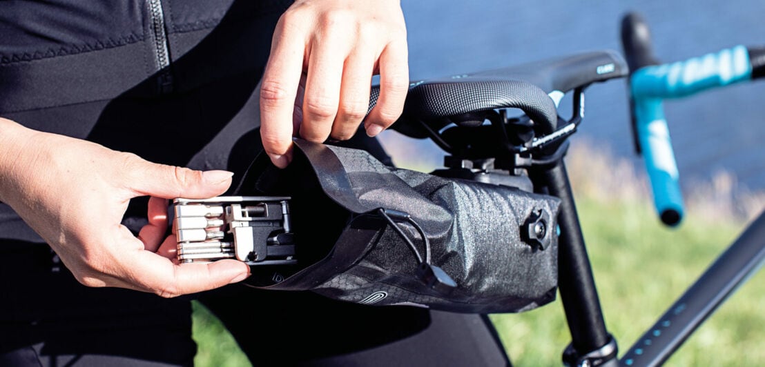 Ein Radfahrer legt ein Multitool-Werkzeug in seine Satteltasche
