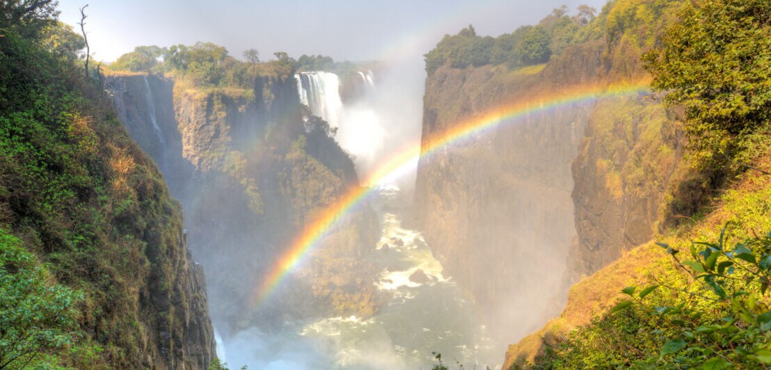 Panoramaansicht der Victoriafälle in Afrika, zwischen deren Felsen ein Regenbogen scheint