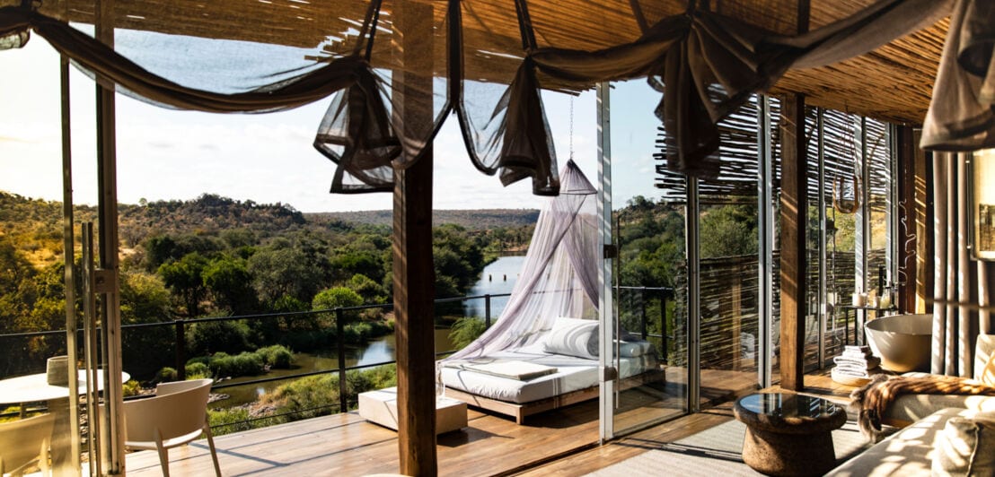 Ein luxuriös ausgestattetes Loft mit Strohdach und offener Fensterfront, die einen Panoramablick auf den Kruger Nationalpark gibt
