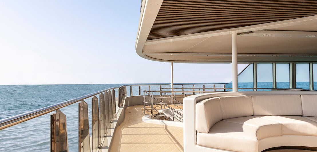 Loungebereich an Deck eines Schiffes mit großer heller Couch, im Hintergrund Meer