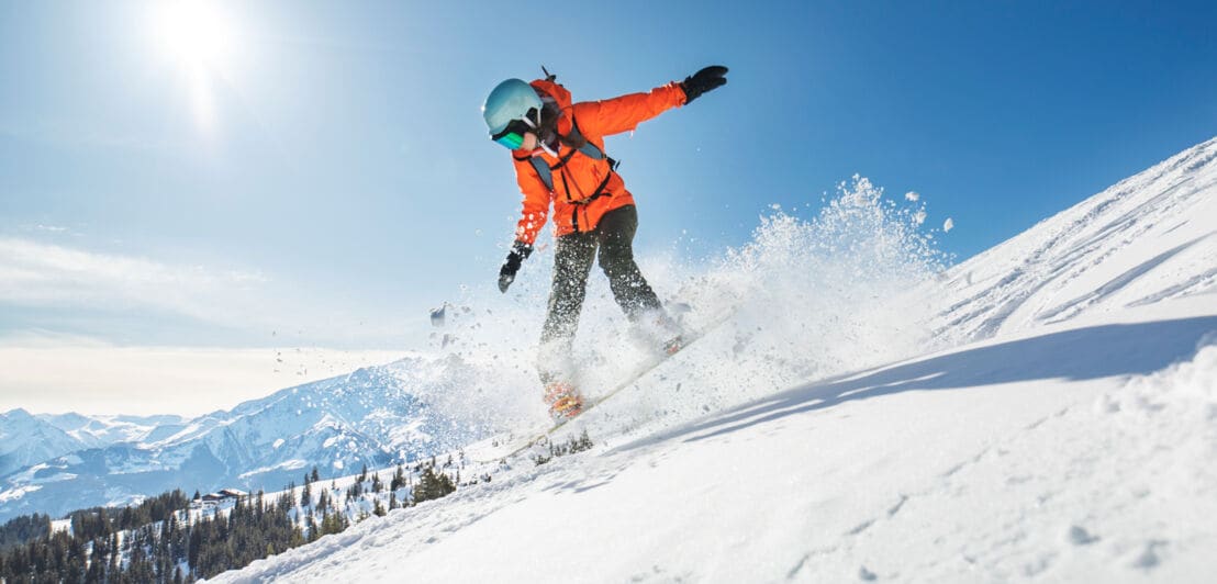 Eine Snowboarderin mit Helm fährt bei Sonnenschein einen Berghang hinunter