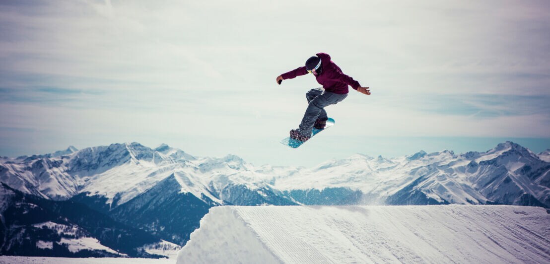 Ein Snowboarder springt über eine Schneeschanze vor Bergpanorama
