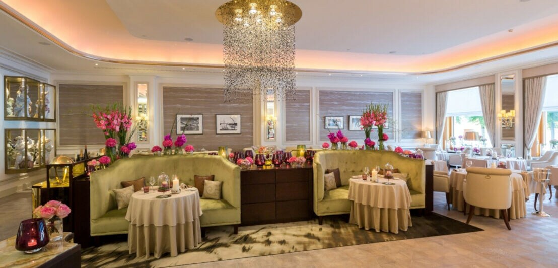 Ein großer Raum mit samtbezogenen Sitzecken, Tischen und rosa Blumen