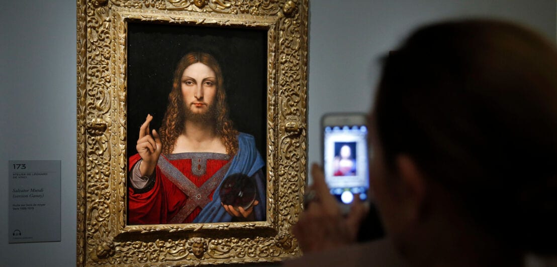Rückansicht einer Person, die mit seinem Smartphone ein Gemälde von Leonardo da Vinci an einer Wand im Museum fotografiert