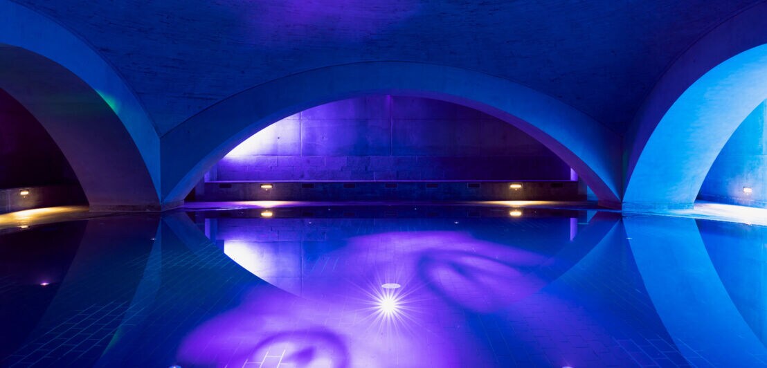 Minimalistisches Wasserbecken mit Rundbögen und blau-violetter Beleuchtung