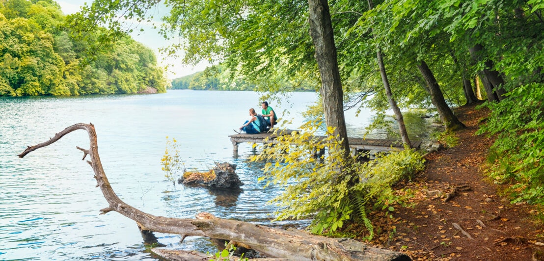 Ein junges Paar sitzt auf einem Steg am See