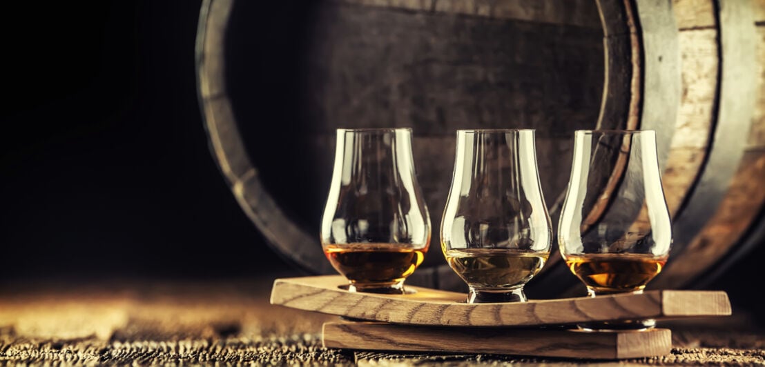 Drei Glencairn-Glöser mit Whisky auf einem Servierbrett vor einem Whiskyfass