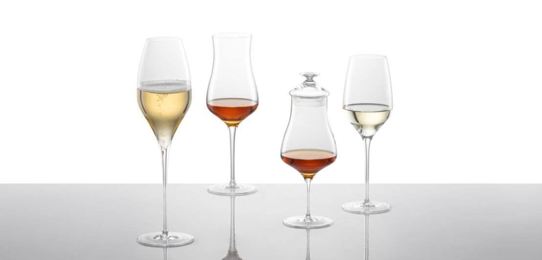 Zwei leicht gefüllte Verkostungsgläser, eins davon mit Deckel, sowie ein klassisches Weißweinglas von Zwiesel Glas stehen auf einer glatten, glänzenden Fläche