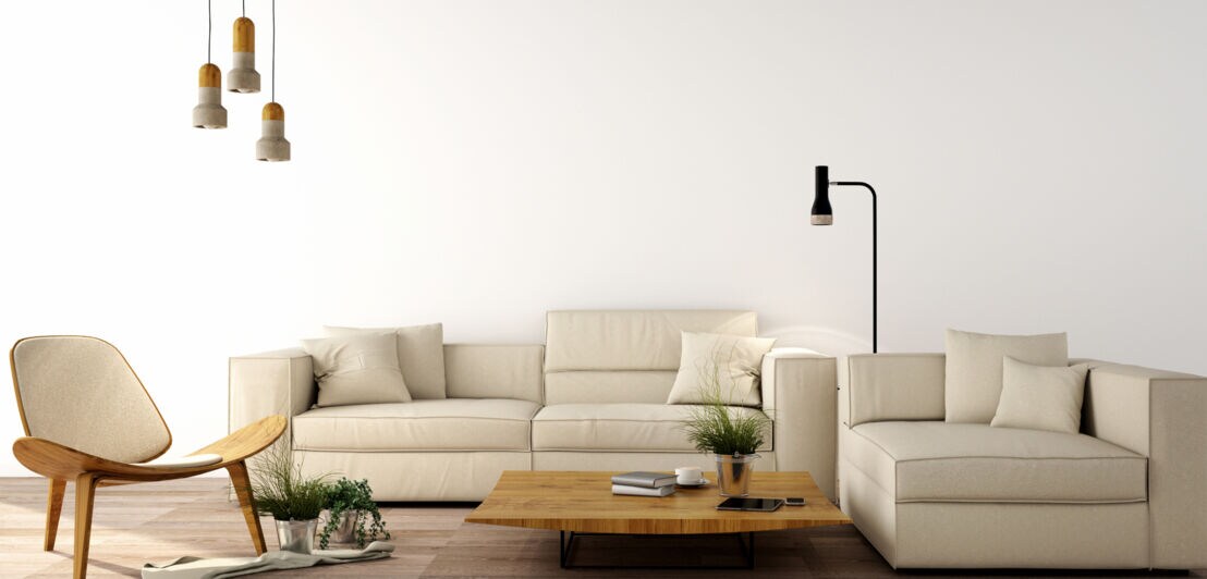 Eine helle Couch sowie ein Sessel aus Holz, dazu ein Couchtisch und Lampen