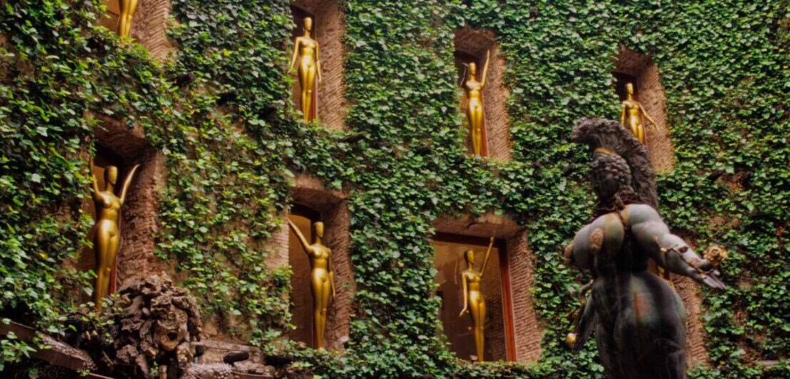 Goldene Skulpturen in Fenstern in einem begrünten Innenhof