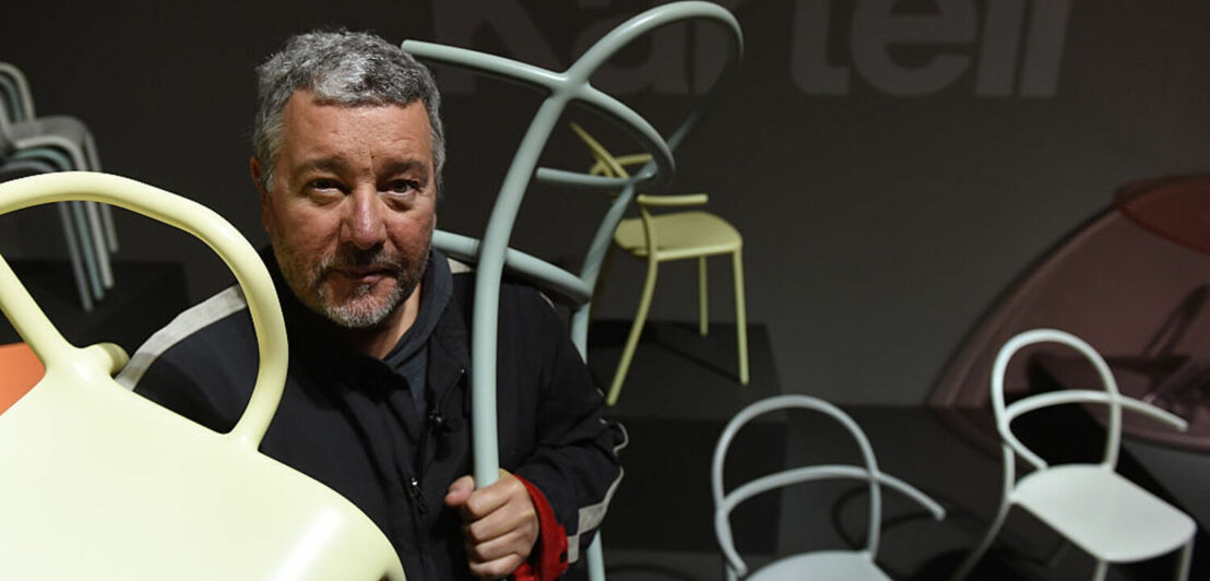 Designer Philippe Starck hält zwei Stühle