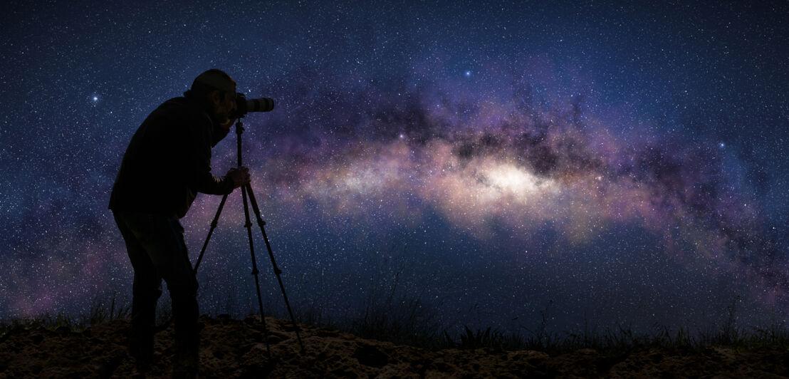 Ein Mann mit einem Stativ fotografiert die Milchstraße.
