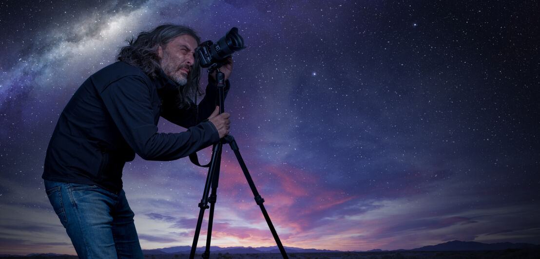 Ein Mann fotografiert am Abend mit einer Kamera auf einem Stativ.