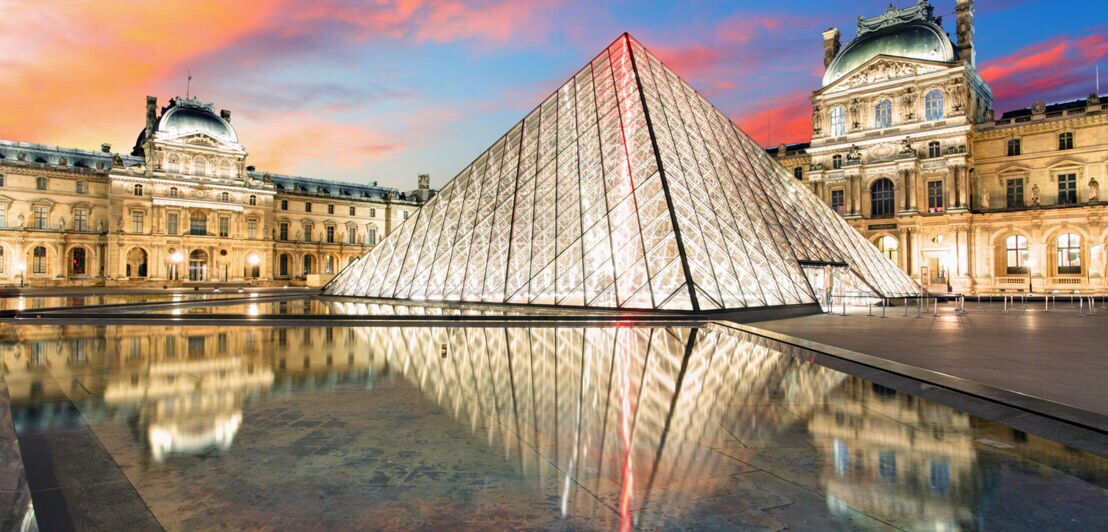 Das dreieckige verglaste Gebäude des Louvre ist hell beleuchtet.
