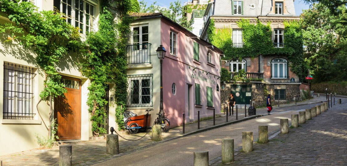 Steile Straße neben historischen, mit Pflanzen berankten Häusern auf dem Montmartre Hügel.