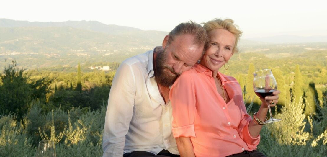 Popstar Sting lehnt sich an seine Ehefrau Trudie, die ein Glas Rotwein hält, vor einer Naturlandschaft in der Toskana