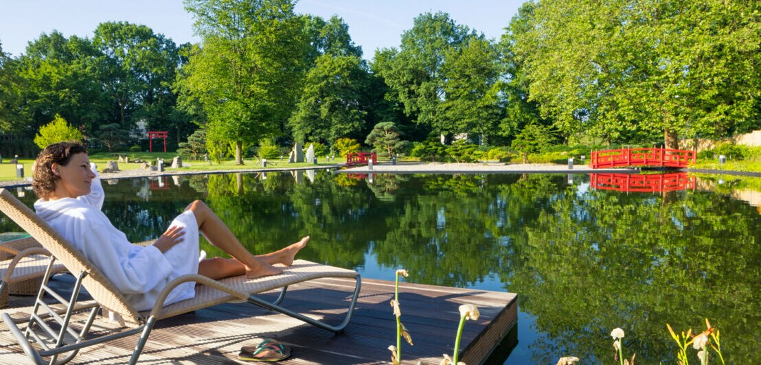 Eine Frau liegt im Bademantel an einem Teich in einem Garten im japanischen Stil