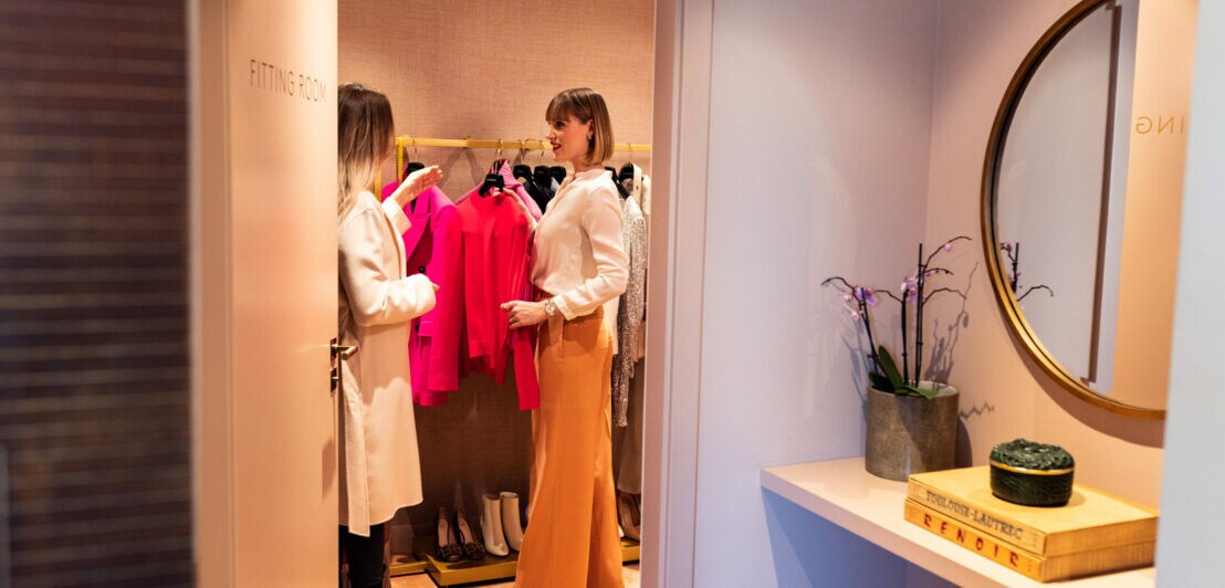 Eine Personal Shopperin präsentiert ihrer Kundin eine Auswahl an Outfits.