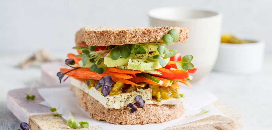 Veganes Sandwich mit Tofu, Salat, Karotten und Paprika auf einem Brett.