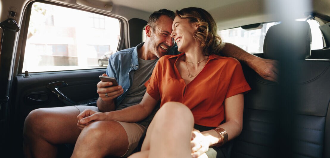 Ein lachendes, mittelaltes Paar in Freizeitkleidung auf dem Rücksitz eines Taxis