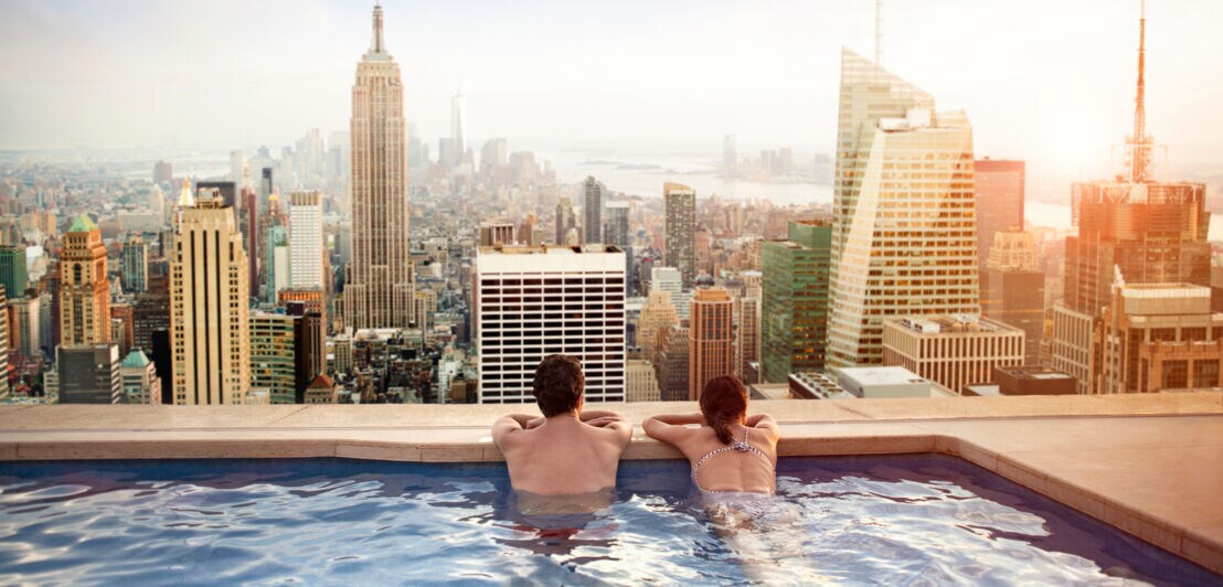 Rückansicht eines Paares in einem Rooftop-Pool, das auf die Skyline von Manhattan blickt