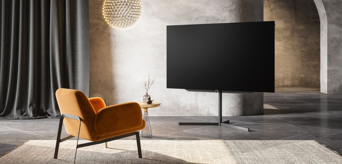 Der Fernseher Loewe bild s.77 in einem Wohnzimmer mit einem Stuhl davor