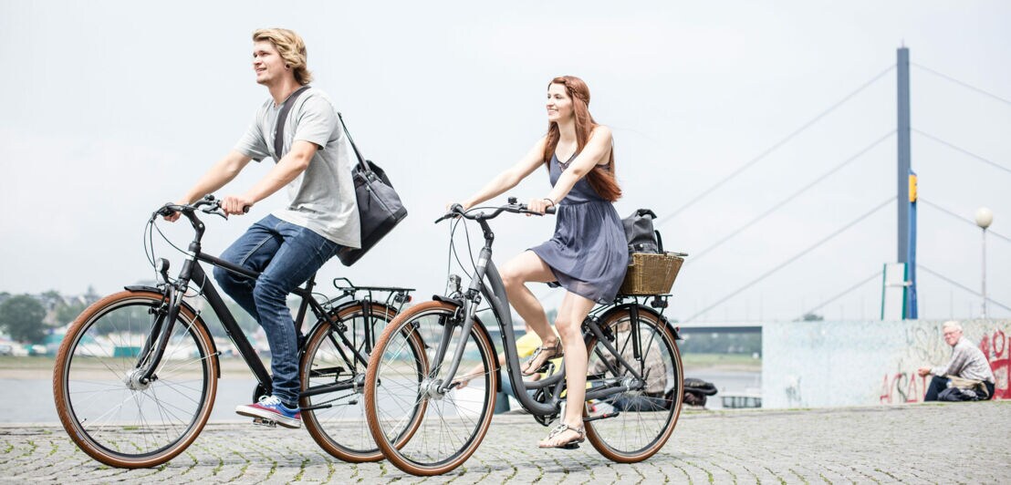 Ein junges Paar fährt an einem Fluß mit dem Rad.