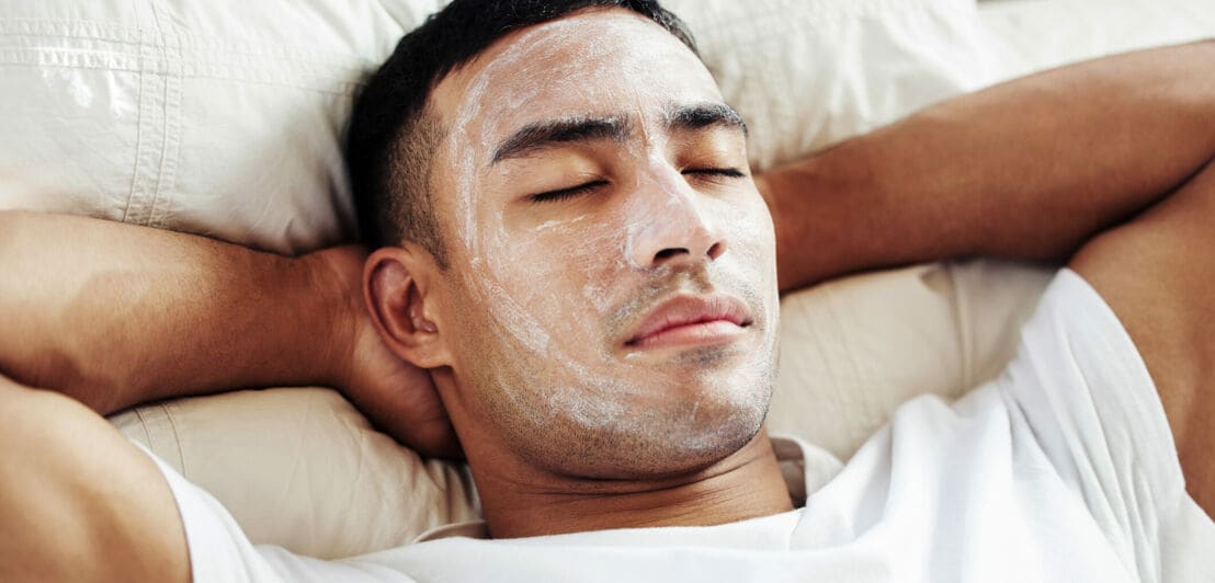 Ein Mann, der eine kosmetische Gesichtsmaske trägt, während er zu Hause auf seinem Bett liegt